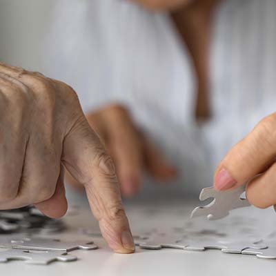 Manos de mujer mayor colocando piezas de un puzle.